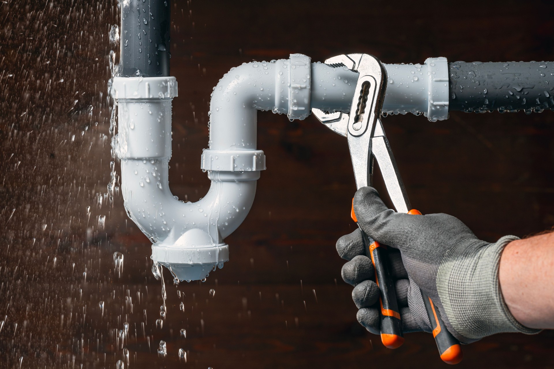 Plumber fixing a water leak in a sink drain siphon.
